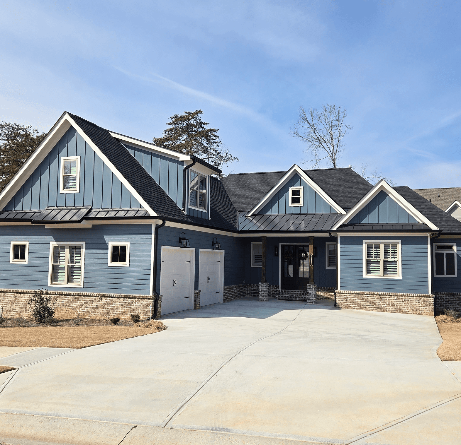 A newly built blue house with a spacious driveway under a clear sky.