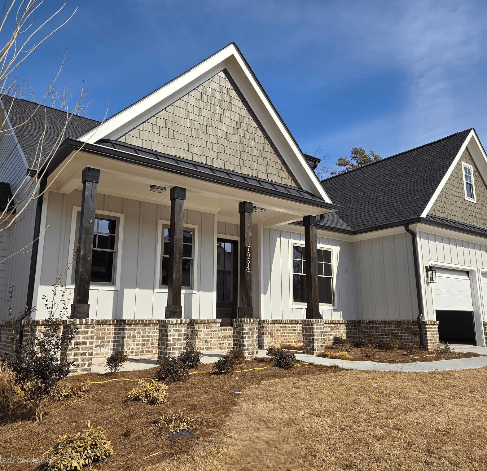 A modern house with a large front porch and stone pillars.