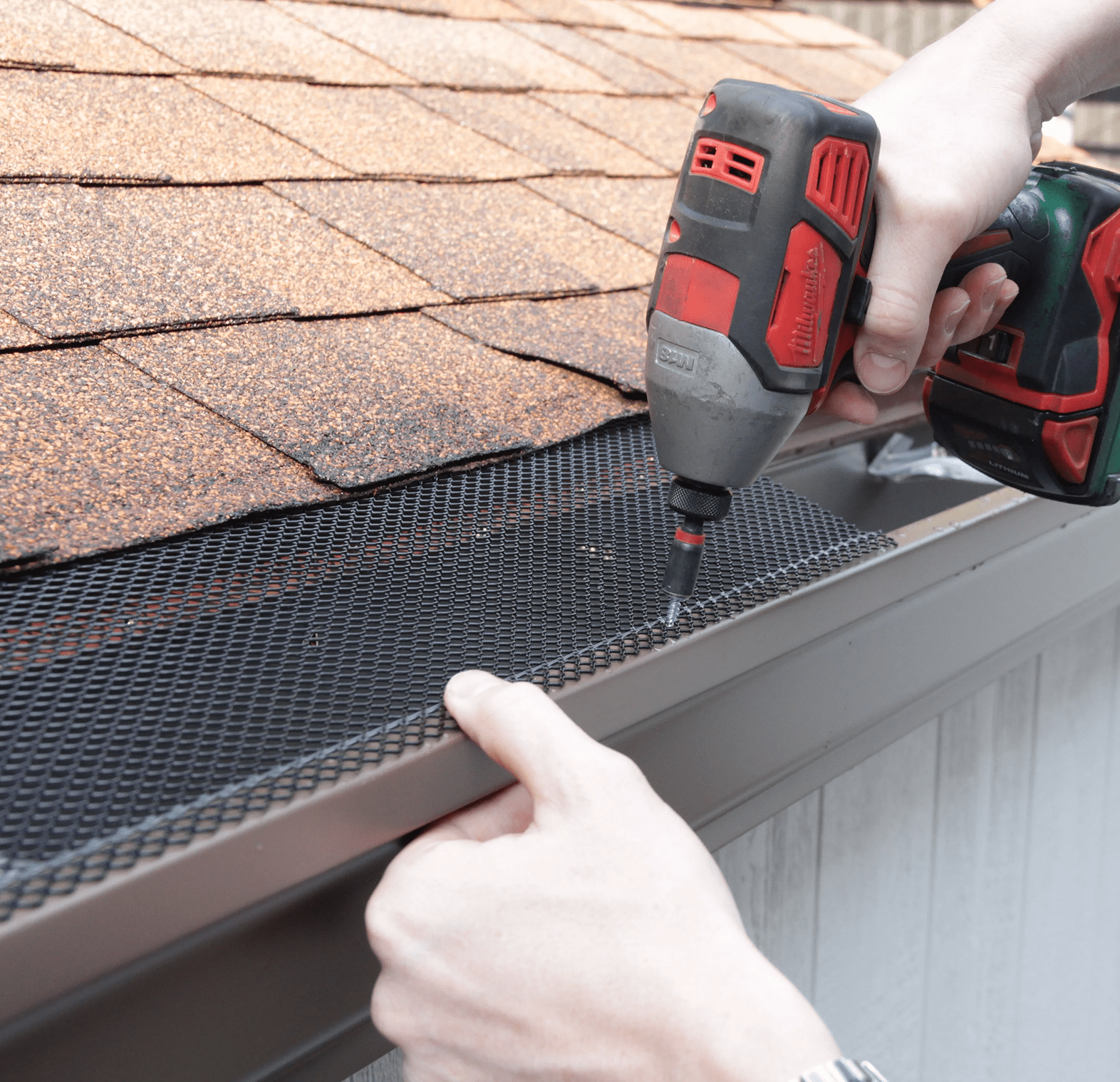 Person installing gutter guard mesh on a roof gutter with a power drill.